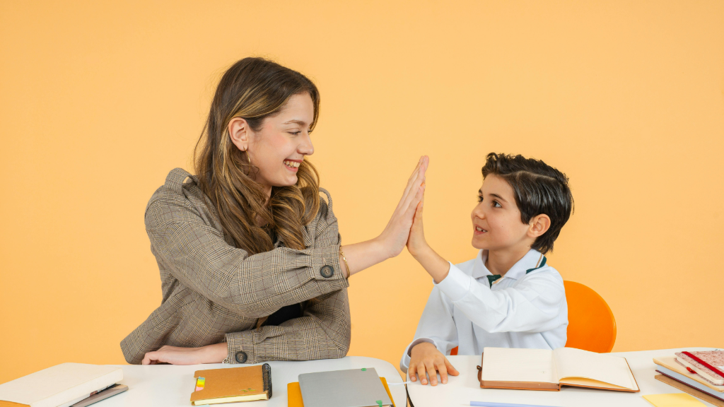 A tutor and a student high-five across a desk during a lesson